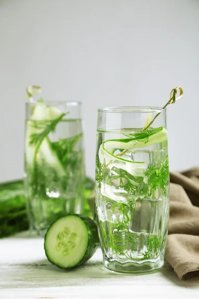 Glasses with fresh organic cucumber water on wooden table, on grey background