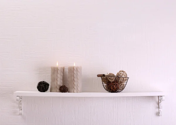 Still life with candles and dried balls on shelf on white wall background