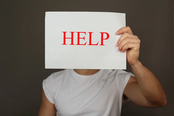 Sheet of paper with Help sign in male hand on dark background