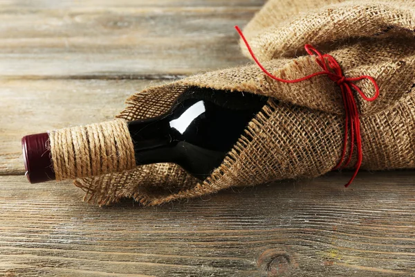 Red wine bottle wrapped in burlap cloth on wooden planks background