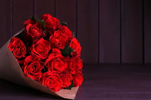 Bouquet of red roses wrapped in paper on wooden background