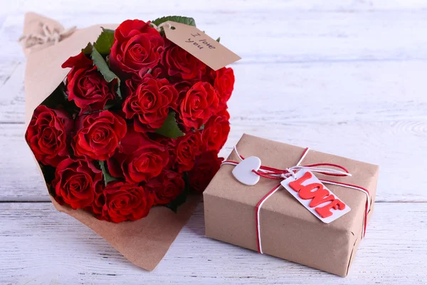 Bouquet of red roses wrapped in paper and present box on wooden background