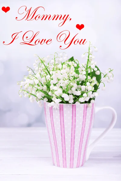 Beautiful flowers in cup on table on light background, Mother's Day concept