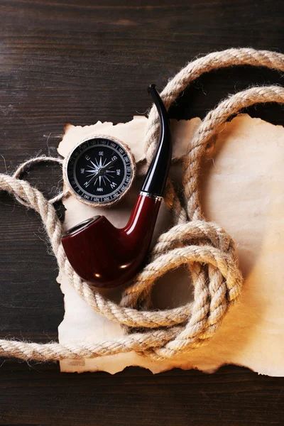 Marine still life pipe, compass, rope and sheet of paper on wooden background