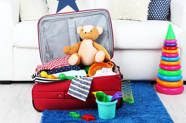 Suitcase packed with clothes and child toys on fur rug and white sofa background