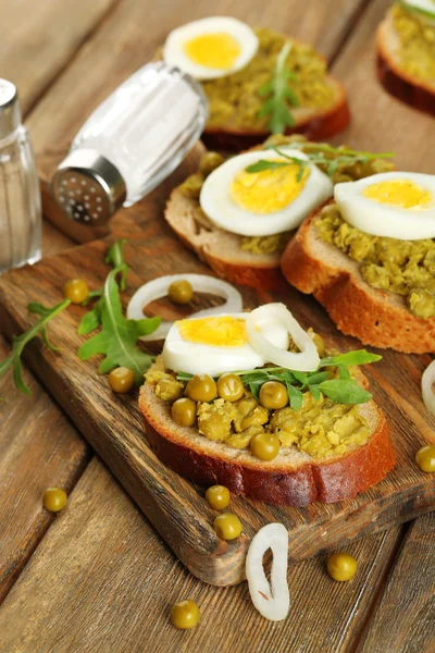 Sandwiches with green peas paste and boiled egg with onion rings and lemon on wooden planks background