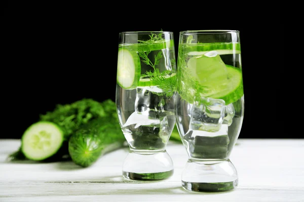 Glasses with fresh organic cucumber water on wooden table, on black background