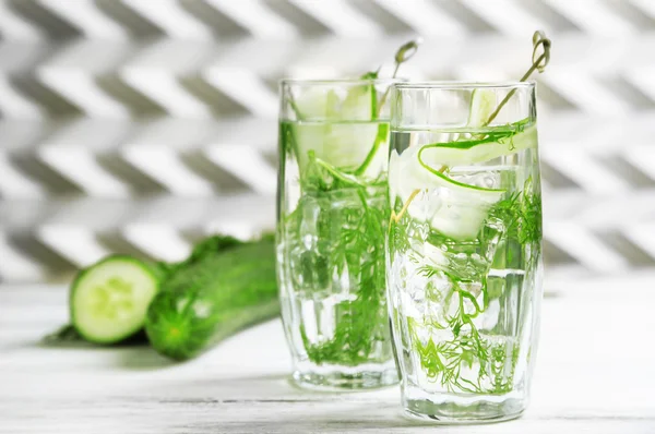 Glasses with fresh organic cucumber water on wooden table, on light background