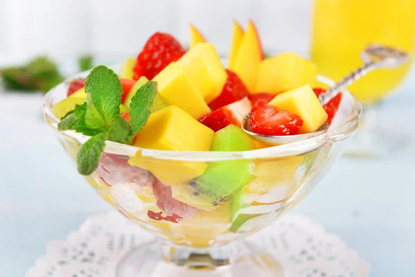Fruit salad in glass bowl with mint and orange juice on color wooden background