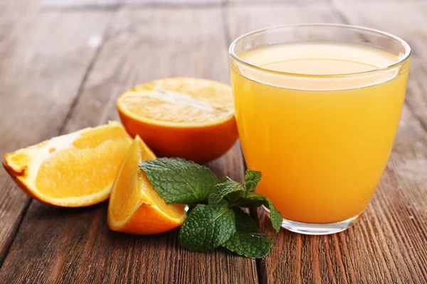 Glass of orange juice with oranges on wooden table close up