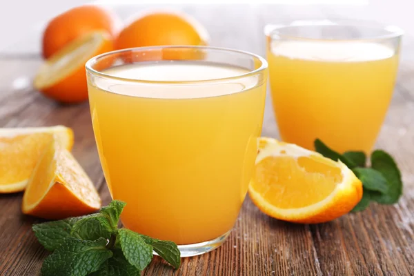 Glasses of orange juice with oranges on wooden table close up