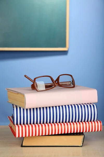 Stack of books with glasses on wooden desk, on colorful wall and blackboard background