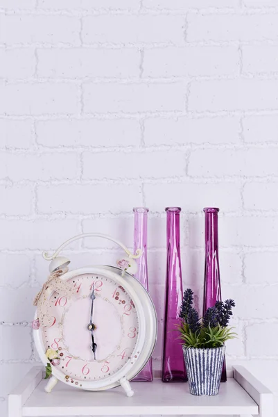 Interior design on tabletop with alarm clock, plant and decorative vases on white brick wall background