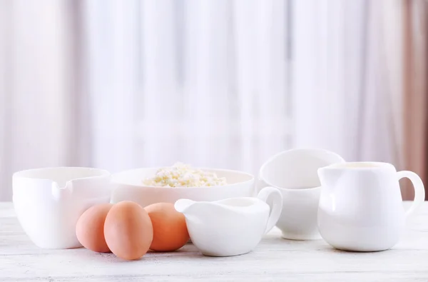 Eggs and dairy products on wooden table on curtain background