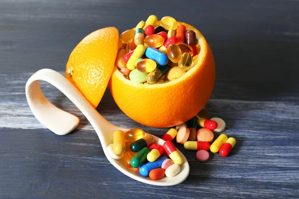 Orange fruit and colorful pills, on color wooden background