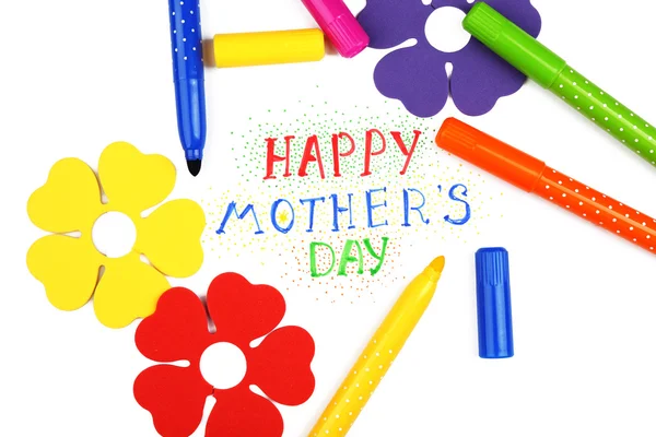 Happy Mothers Day message written on paper with markers and decorative flowers close up
