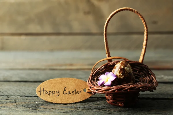 Bird egg in wicker basket with decorative flowers on wooden background