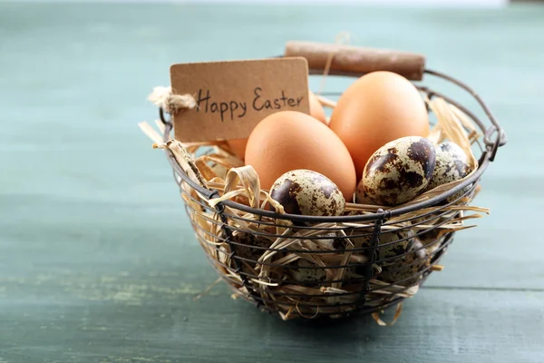 Bird eggs in wicker basket with decorative flowers on color wooden background