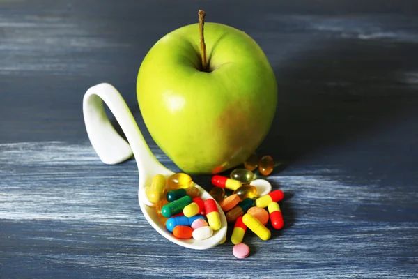 Apple and colorful pills, on color wooden background