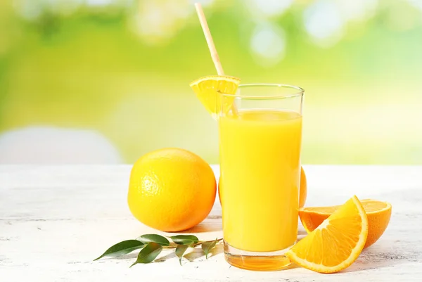 Glass of orange juice with straw and slices on wooden table and bright background