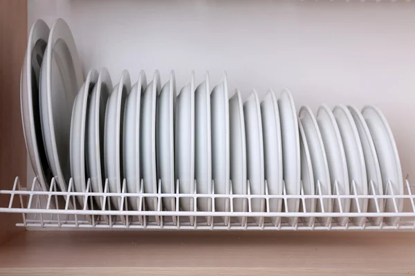 Clean plates drying on metal dish rack on shelf