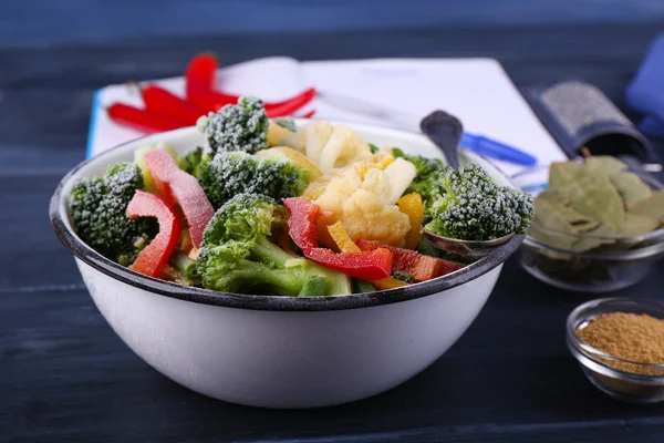 Frozen vegetables and blank notebook, on wooden table background