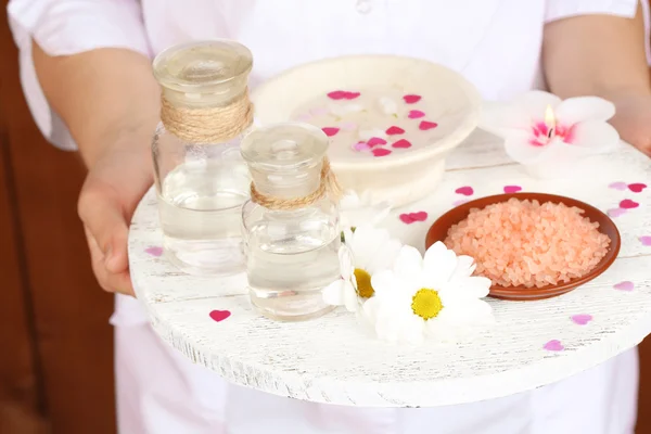 Beauty therapist holding tray of spa treatments, close-up, on wooden wall background