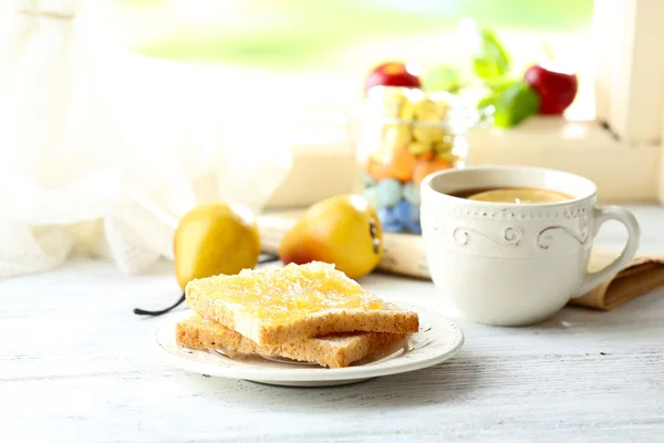 Toasts with honey on plate with cup of tea on light background