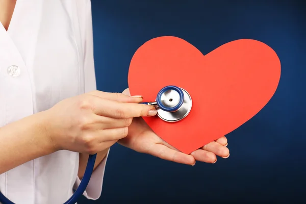 Doctor hands with heart and stethoscope on blue background