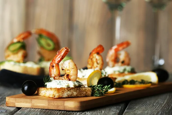 Appetizer canape with shrimp and olives on cutting board on table close up