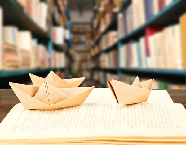 Open book with paper ships on bookshelves background