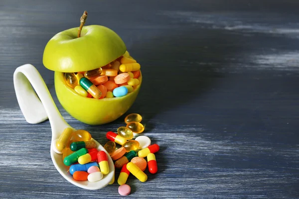 Apple and colorful pills, on color wooden background