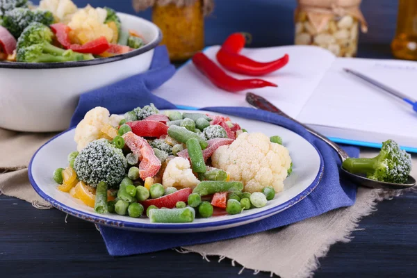 Frozen vegetables on plate on napkin, on wooden table background