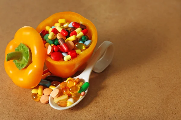 Orange pepper and colorful pills, on wooden background