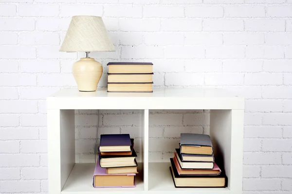 Wooden shelf with books and lamp on brick wall background