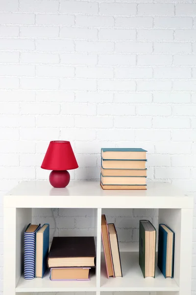 Wooden shelf with books and lamp on brick wall background