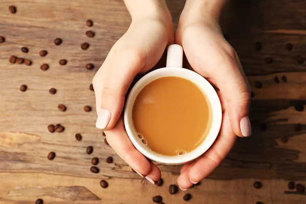 Female hands holding cup with coffee beans on wooden table background