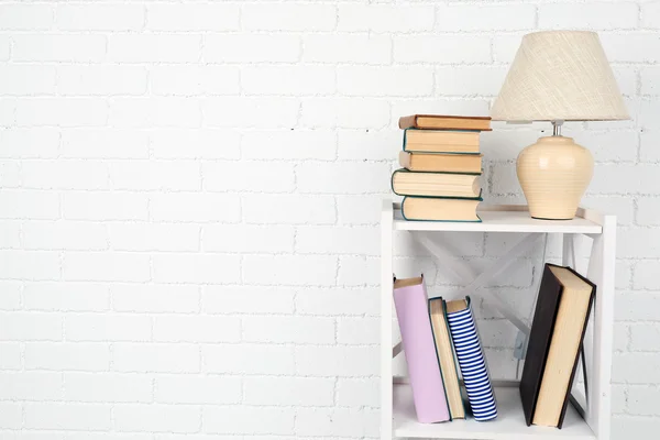 Wooden shelf with books and lamp on brick wall background