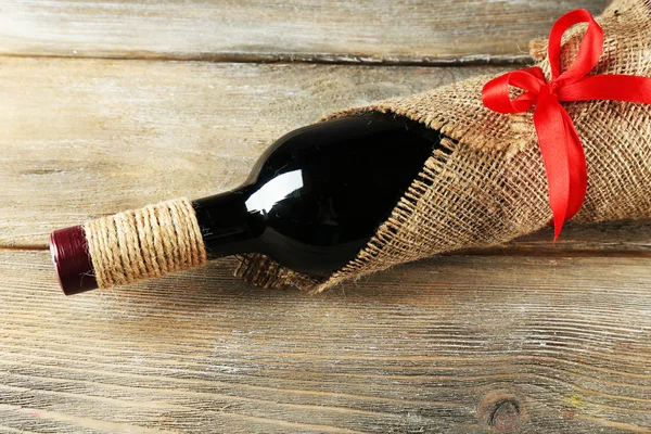 Red wine bottle wrapped in burlap cloth on wooden planks background