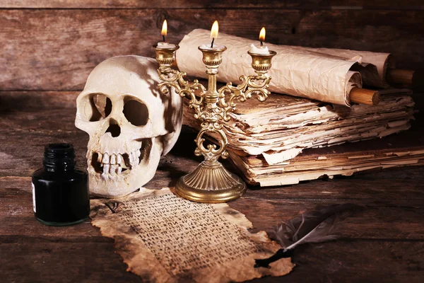 Still life with human skull, retro book and quill on wooden table, closeup