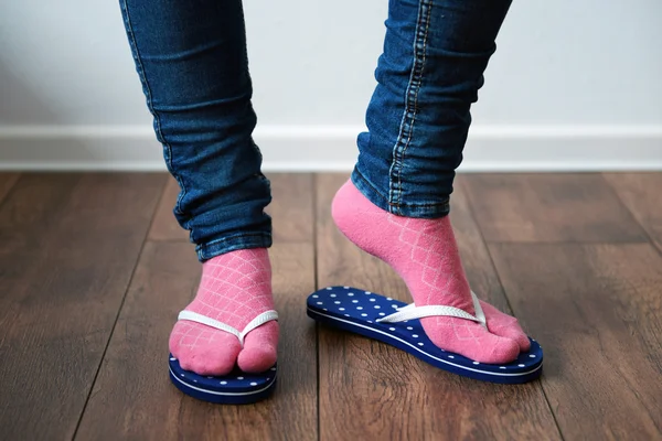 Female feet in socks with pink flip-flops, on floor background