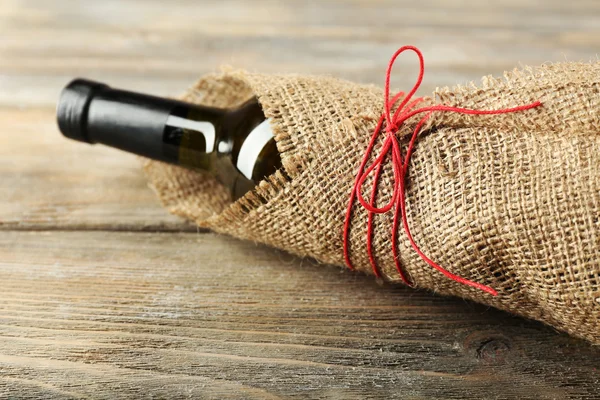 Wine bottle wrapped in burlap cloth on wooden planks background