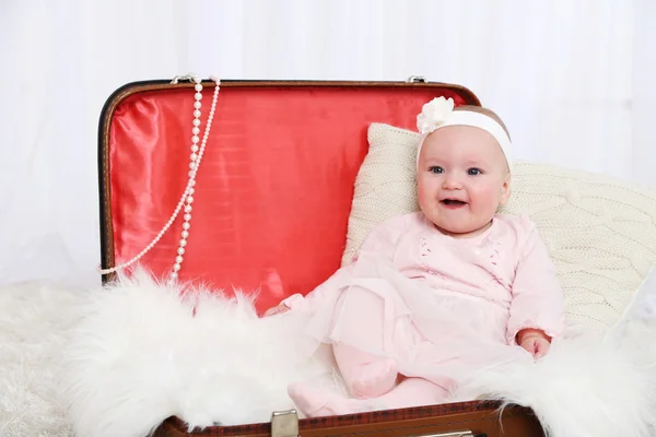 Cute baby girl sitting in big suitcase on carpet, on light background
