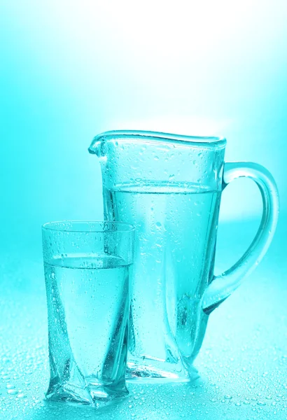 Glass pitcher and glass of water on blue background