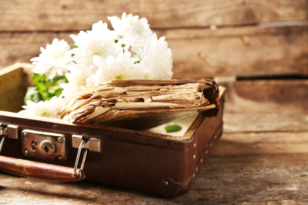 Old wooden suitcase with old books and flowers on wooden background