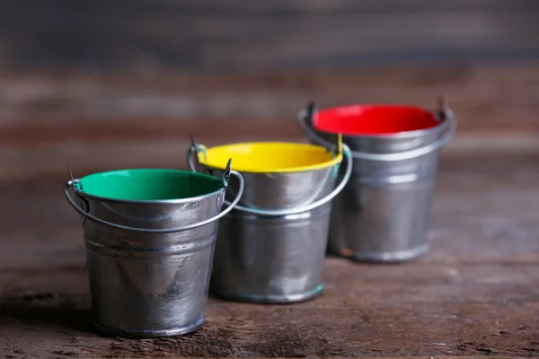 Metal buckets with colorful paint on wooden background