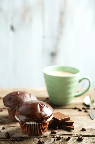 Tasty homemade chocolate muffins and cup of coffee on wooden table, on light background