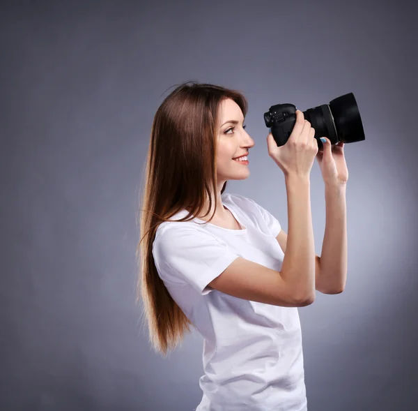 Young female photographer taking photos on grey background