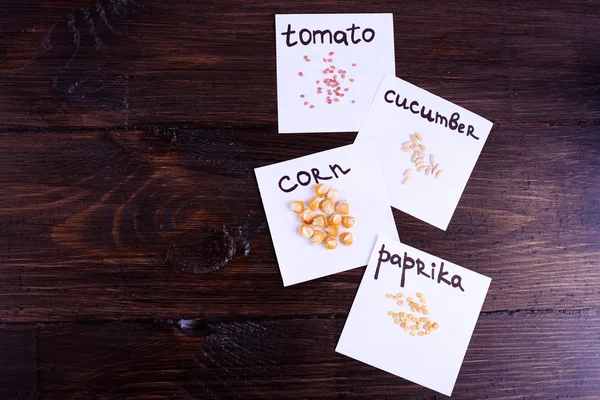 Different seeds on pieces of paper on wooden background