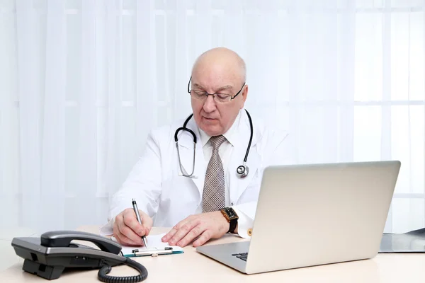 Portrait of professional doctor at table in his office on white curtain background